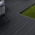 Dark composite decking next to grass with chair leg.