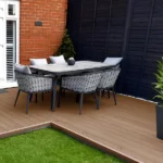 Outdoor dining set on brown composite decking and grass.