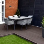 Outdoor dining set on dark composite decking and grass.